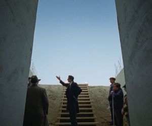 Still from the Brutalist film - Adrian Brody, flanked by concrete columns on both sides gestures to the left.