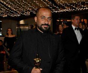 Hamdan Ballal in a black suit with his Oscar at 2025's Academy Awards. Some kind of Oscar reception is going on behind him,